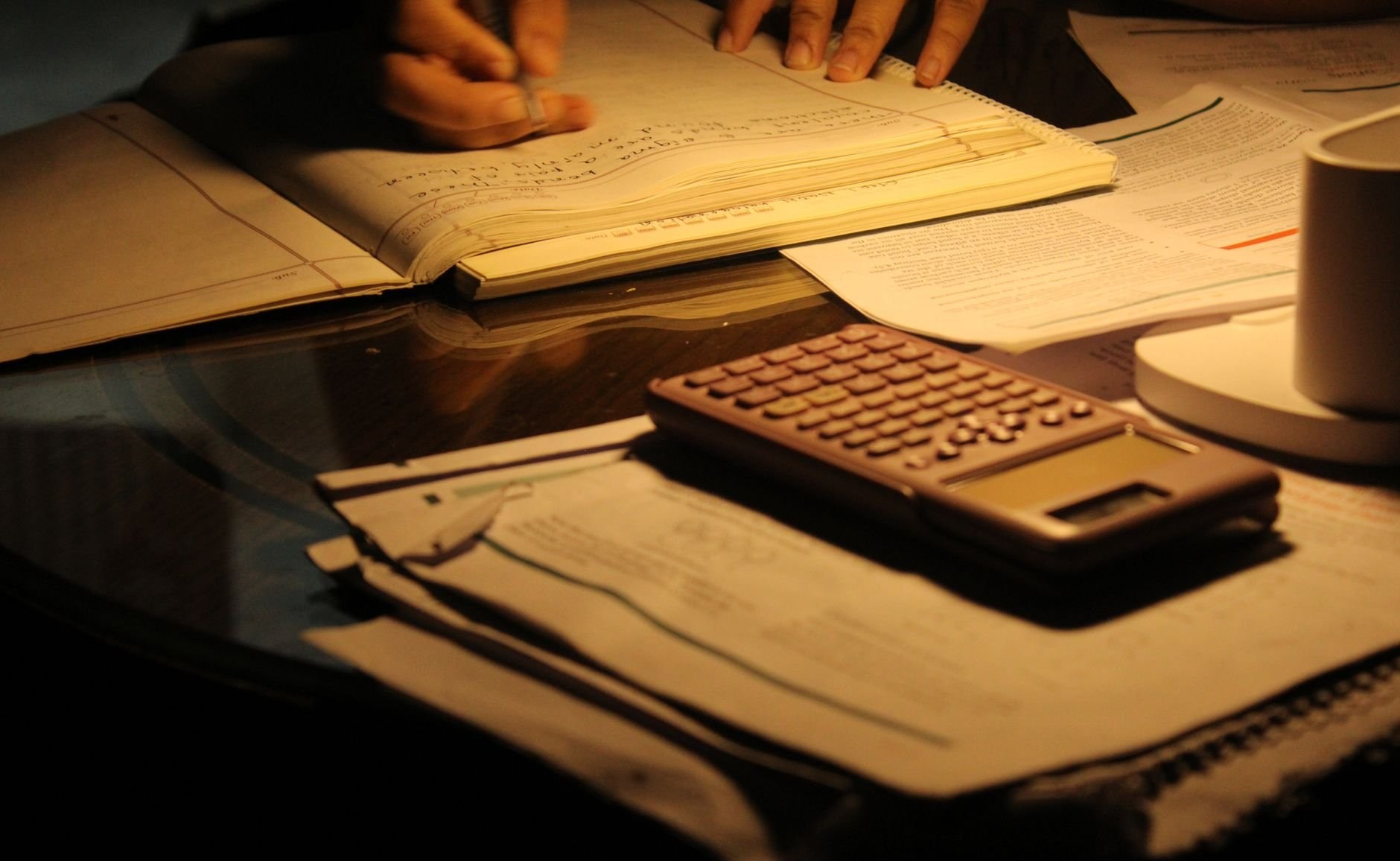 Sessão de estudo noturna e concentrada, com livros abertos e uma calculadora sobre uma mesa com pouca luz.